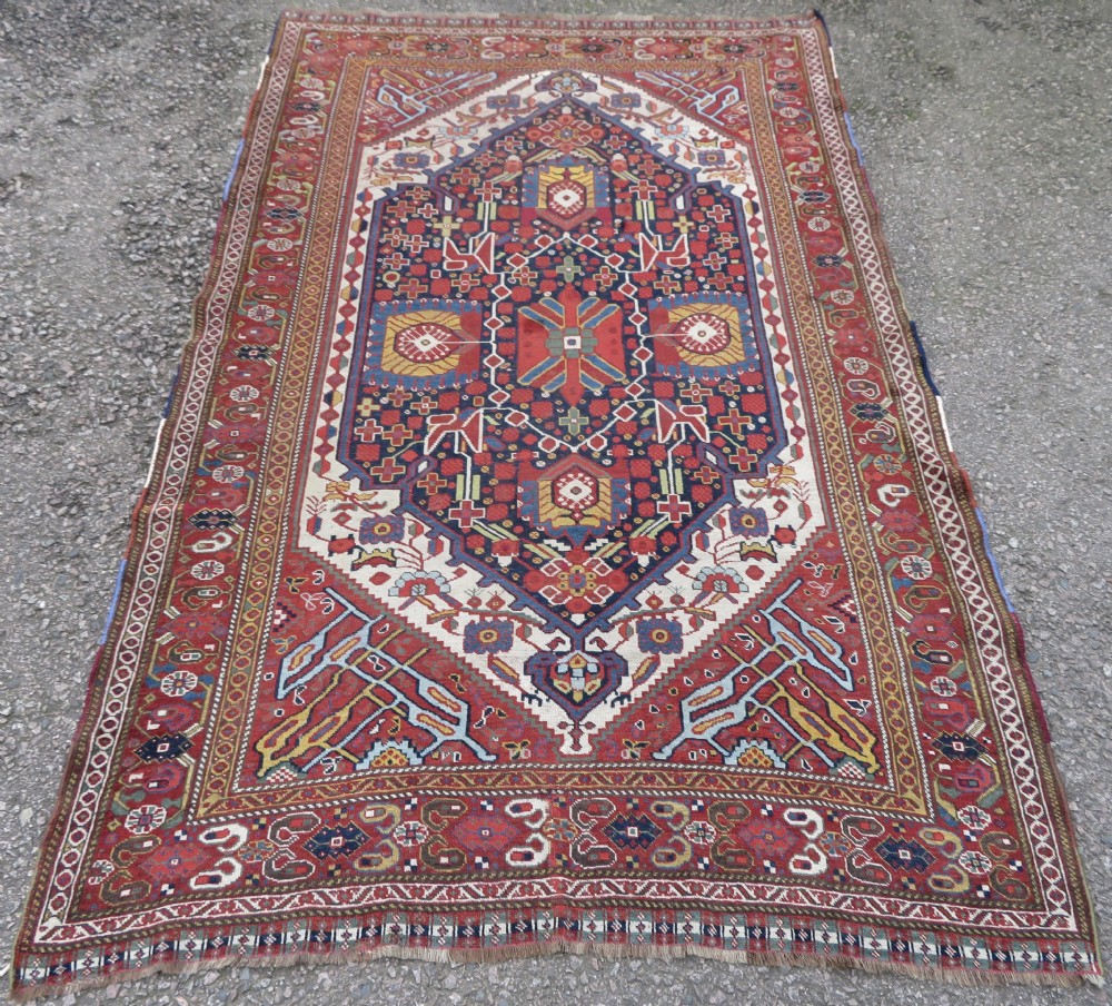 An antique hand-woven Persian Khamseh wool rug featuring a central geometric medallion with tribal bird motifs in red, navy blue, and ivory tones. View XXIV