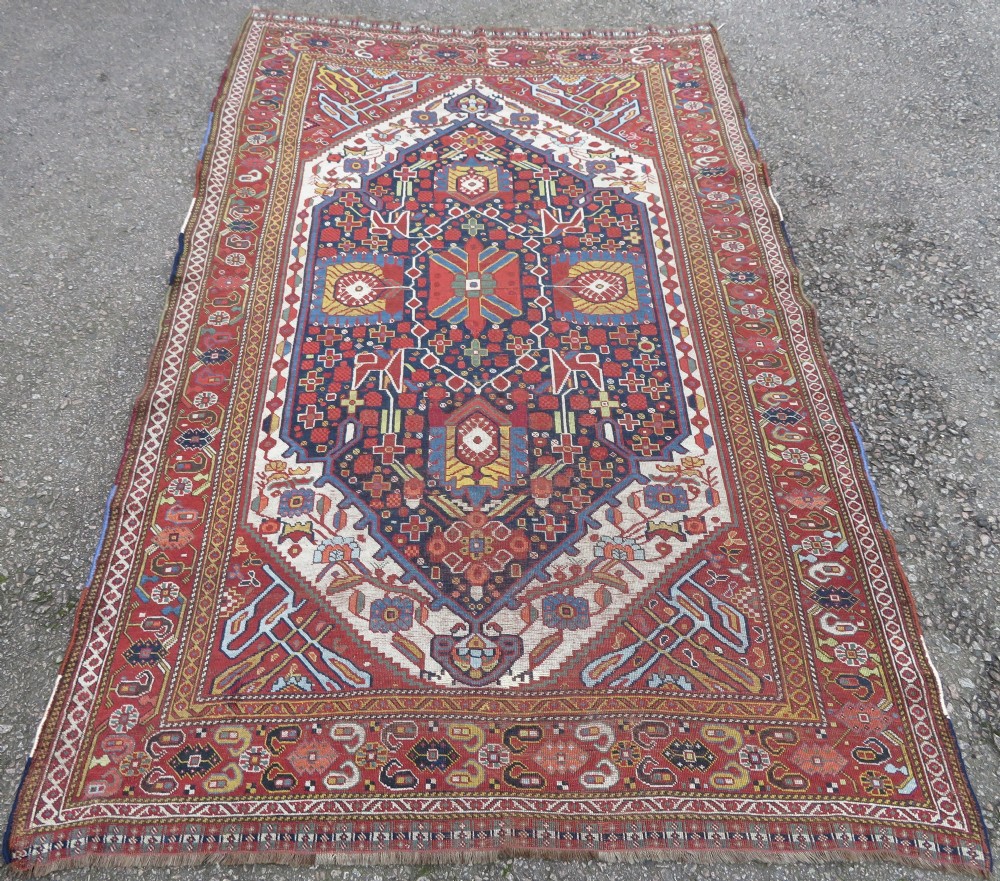 An antique hand-woven Persian Khamseh wool rug featuring a central geometric medallion with tribal bird motifs in red, navy blue, and ivory tones. View XXV