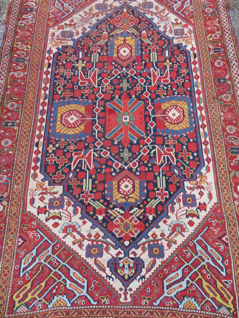 An antique hand-woven Persian Khamseh wool rug featuring a central geometric medallion with tribal bird motifs in red, navy blue, and ivory tones. View XXVI