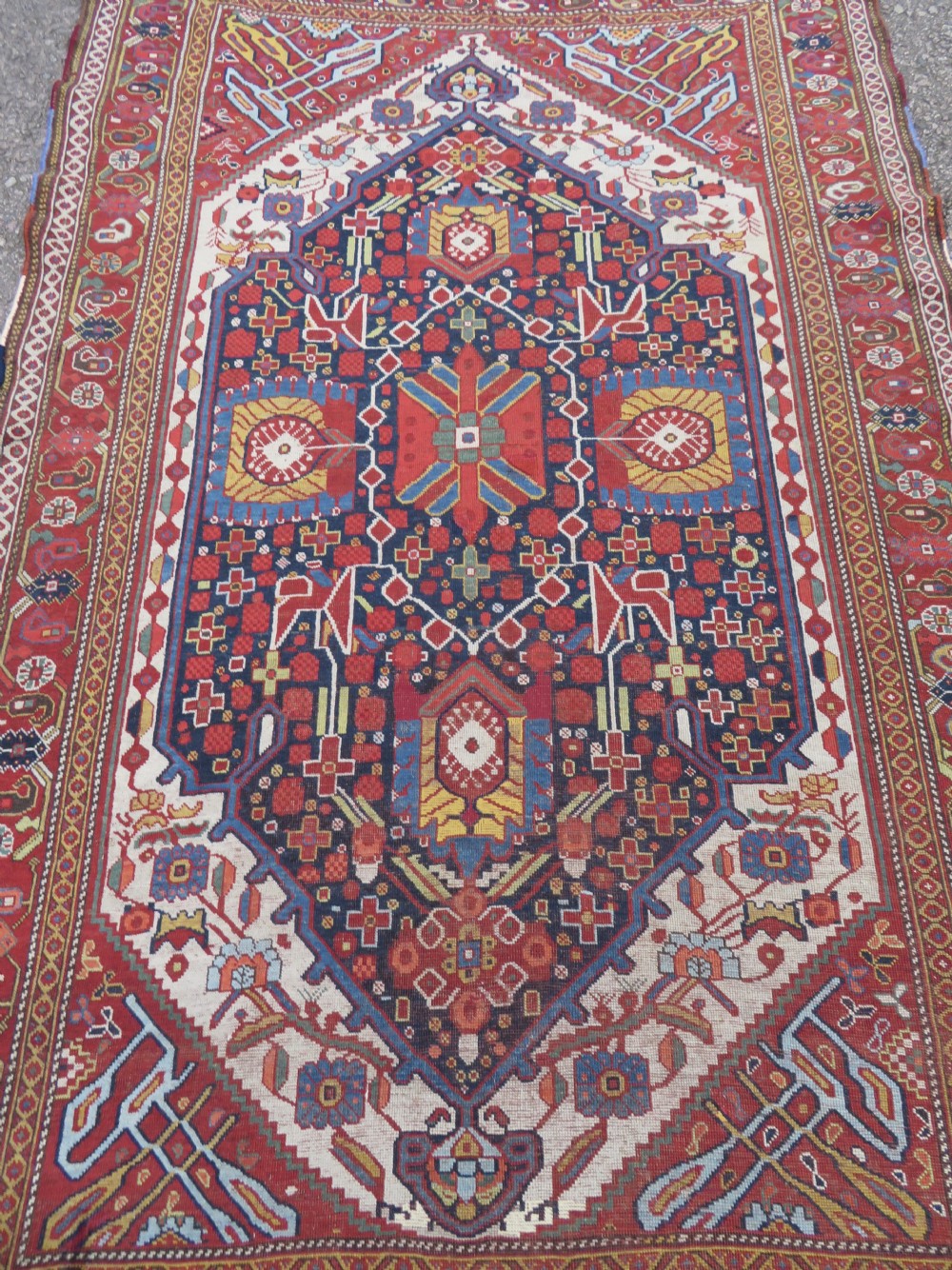 An antique hand-woven Persian Khamseh wool rug featuring a central geometric medallion with tribal bird motifs in red, navy blue, and ivory tones. View XXVII