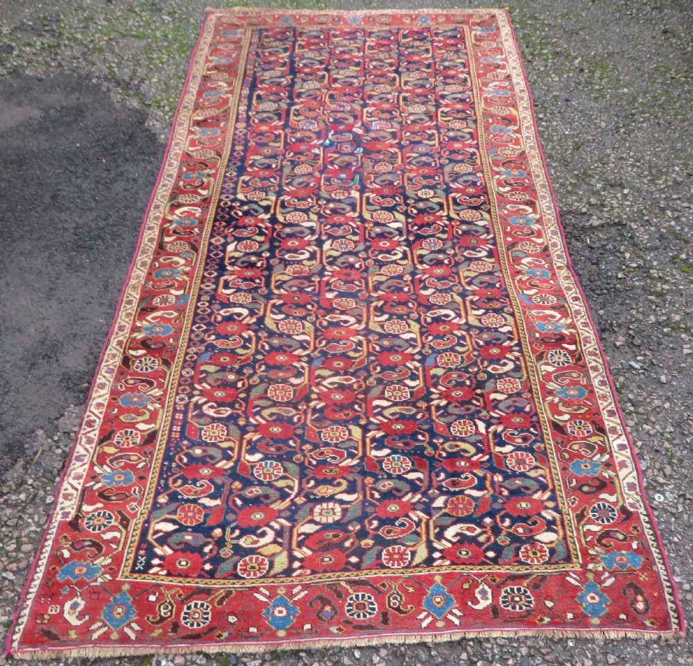 A long hand-knotted Persian Khamseh rug with a navy blue field filled with repeating floral and boteh motifs, framed by a patterned red border.