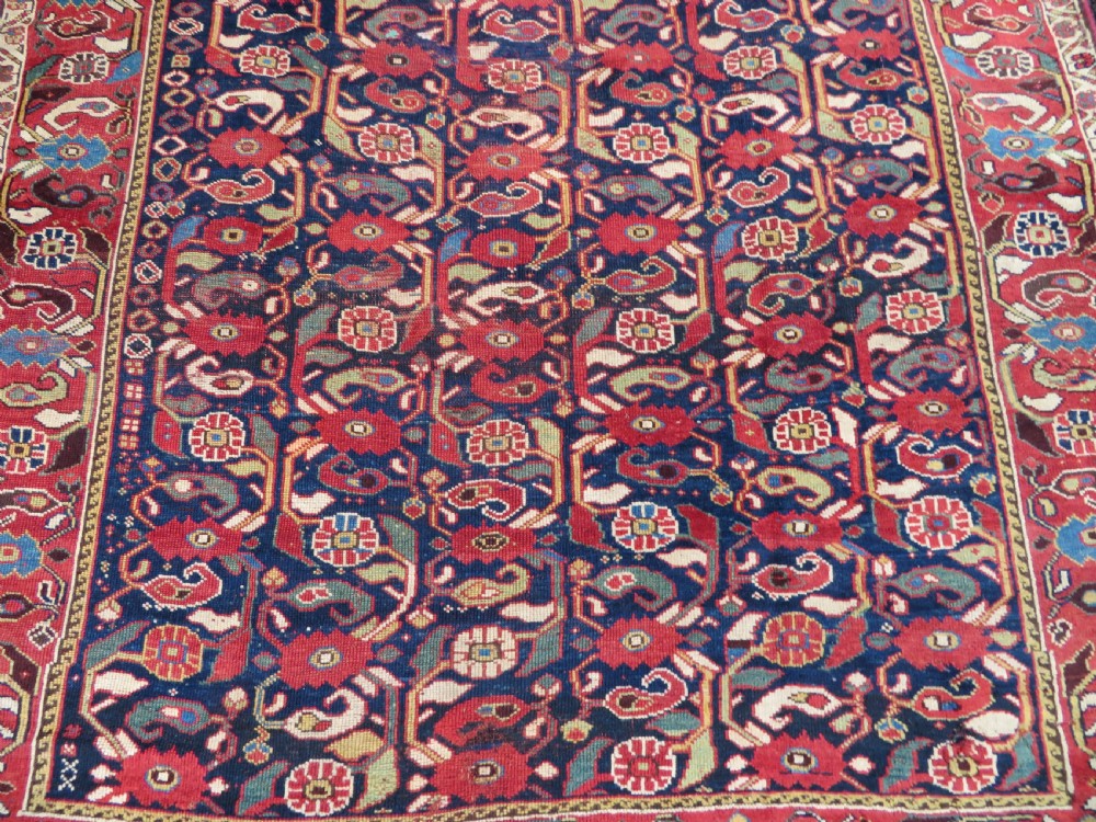 A long hand-knotted Persian Khamseh rug with a navy blue field filled with repeating floral and boteh motifs, framed by a patterned red border. View V