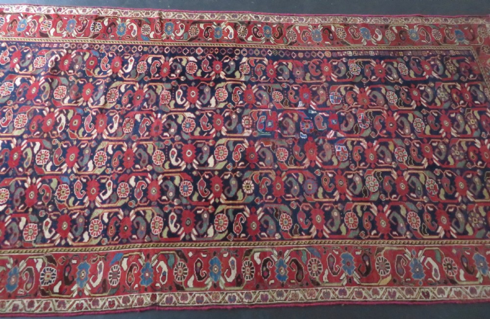 A long hand-knotted Persian Khamseh rug with a navy blue field filled with repeating floral and boteh motifs, framed by a patterned red border. View XXVI