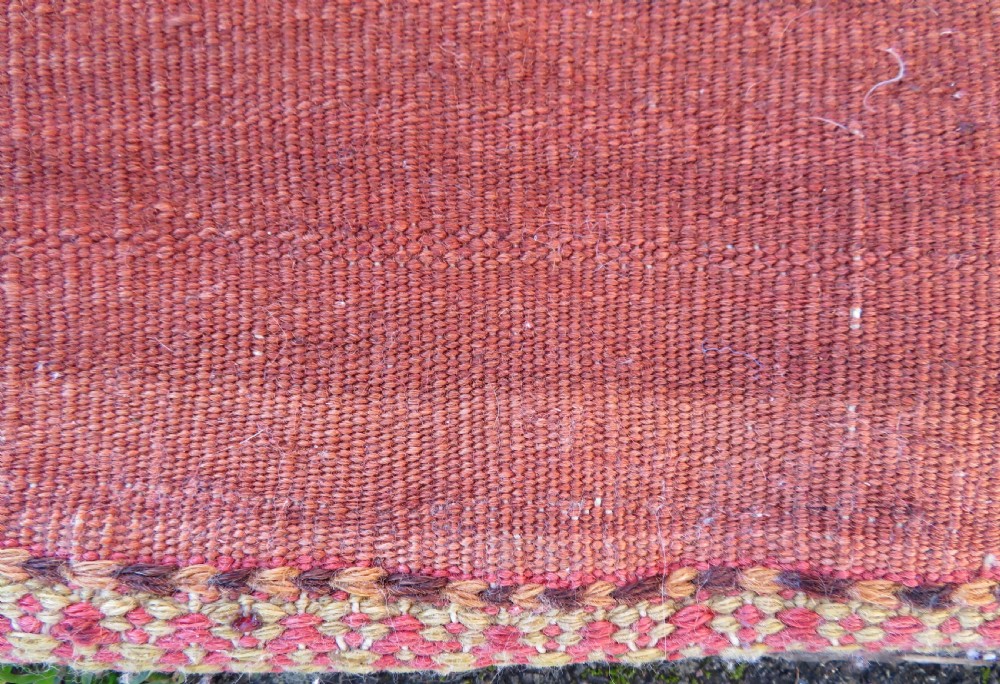 A square antique handwoven wool saddle bag face featuring a central red geometric diamond motif on a navy blue field with patterned cream borders and woven loops along the top edge. View XII