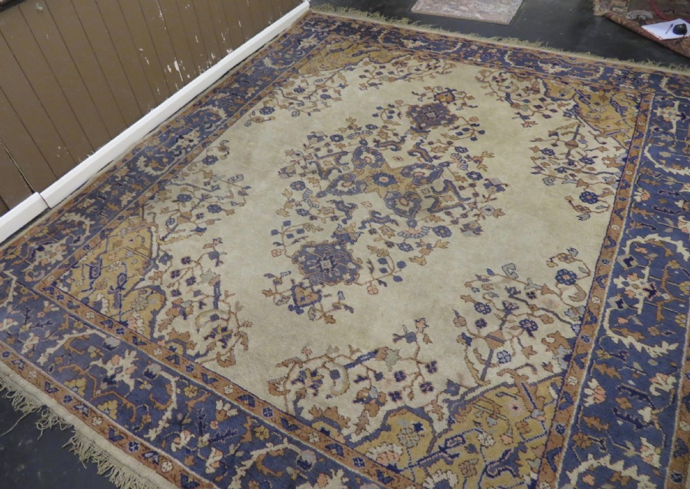 An antique hand-knotted wool area carpet featuring an ivory central field, detailed central medallion, corner spandrels, and a broad indigo floral border. View II