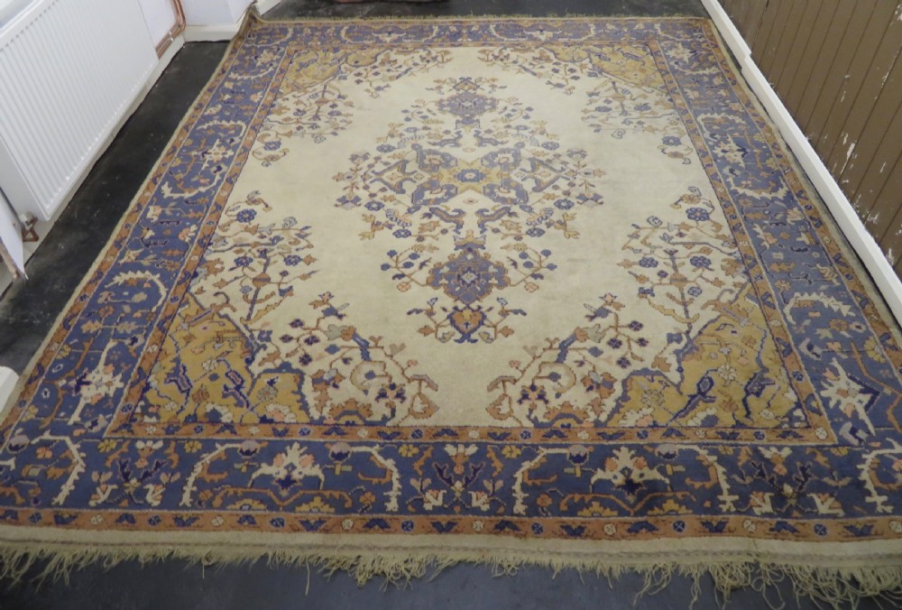 An antique hand-knotted wool area carpet featuring an ivory central field, detailed central medallion, corner spandrels, and a broad indigo floral border. View III