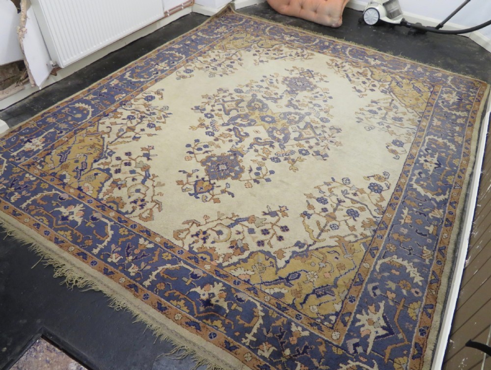 An antique hand-knotted wool area carpet featuring an ivory central field, detailed central medallion, corner spandrels, and a broad indigo floral border. View IV