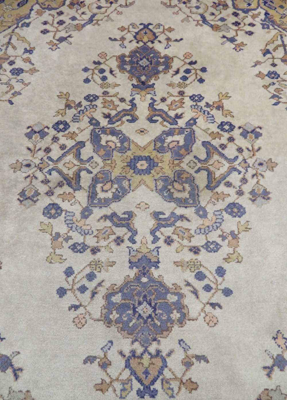 An antique hand-knotted wool area carpet featuring an ivory central field, detailed central medallion, corner spandrels, and a broad indigo floral border. View VI