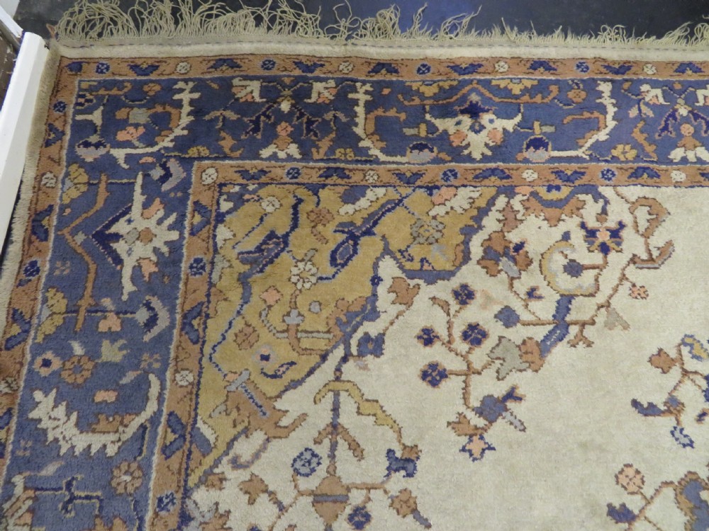 An antique hand-knotted wool area carpet featuring an ivory central field, detailed central medallion, corner spandrels, and a broad indigo floral border. View VII