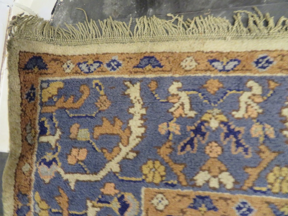 An antique hand-knotted wool area carpet featuring an ivory central field, detailed central medallion, corner spandrels, and a broad indigo floral border. View X