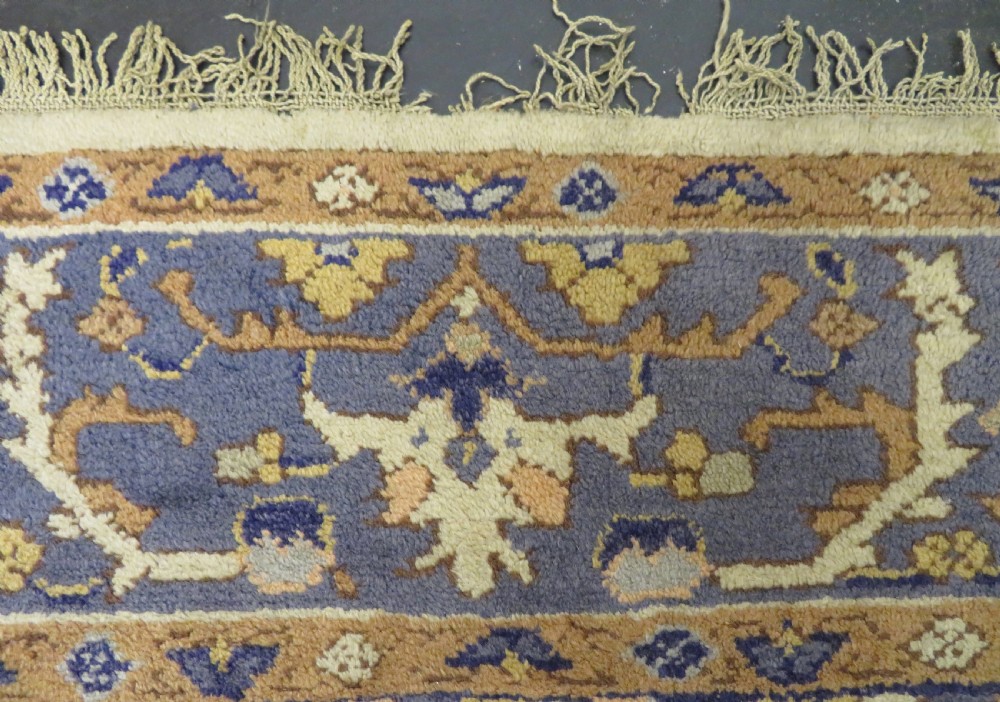 An antique hand-knotted wool area carpet featuring an ivory central field, detailed central medallion, corner spandrels, and a broad indigo floral border. View XI