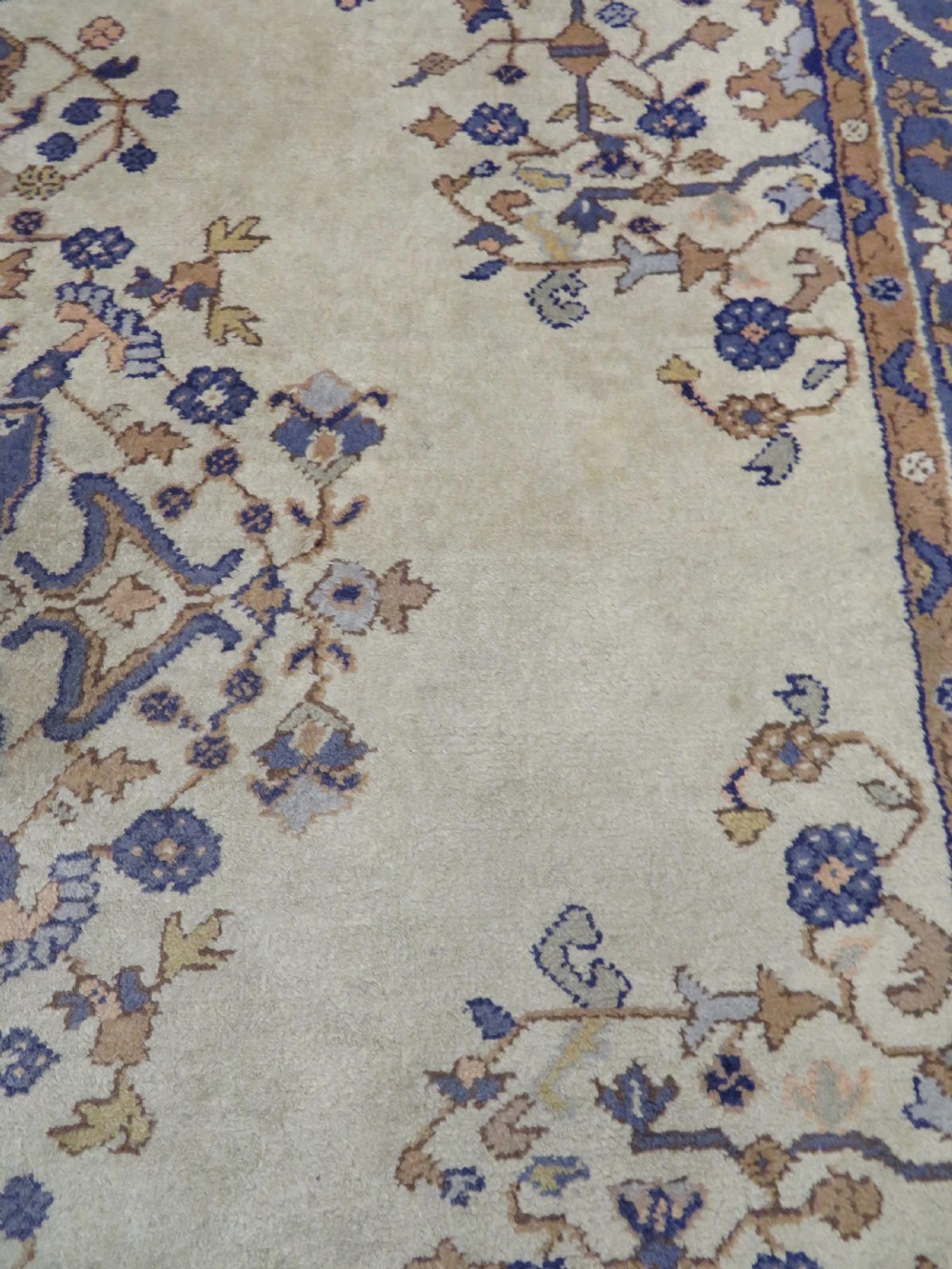 An antique hand-knotted wool area carpet featuring an ivory central field, detailed central medallion, corner spandrels, and a broad indigo floral border. View XV