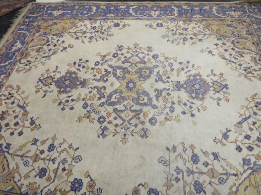 An antique hand-knotted wool area carpet featuring an ivory central field, detailed central medallion, corner spandrels, and a broad indigo floral border. View XVIII