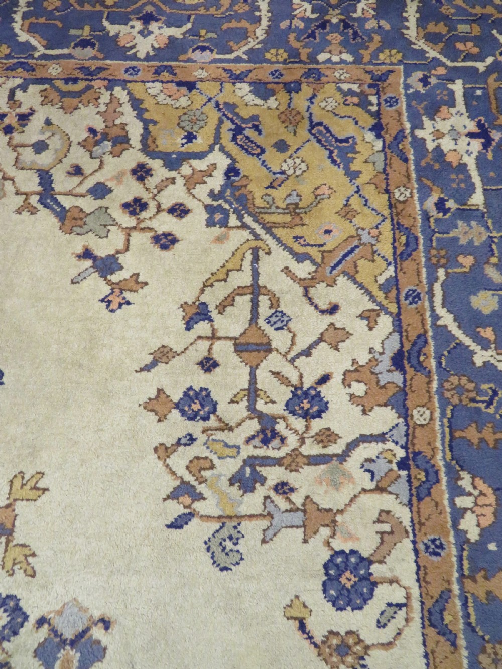 An antique hand-knotted wool area carpet featuring an ivory central field, detailed central medallion, corner spandrels, and a broad indigo floral border. View XX