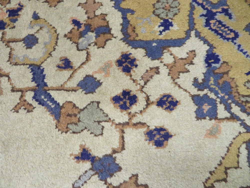 An antique hand-knotted wool area carpet featuring an ivory central field, detailed central medallion, corner spandrels, and a broad indigo floral border. View XXI