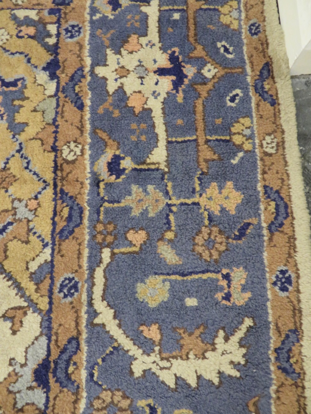 An antique hand-knotted wool area carpet featuring an ivory central field, detailed central medallion, corner spandrels, and a broad indigo floral border. View XXII