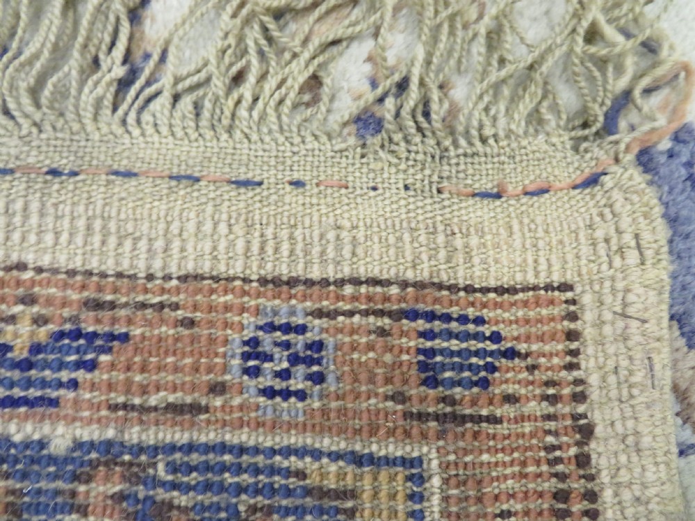An antique hand-knotted wool area carpet featuring an ivory central field, detailed central medallion, corner spandrels, and a broad indigo floral border. View XXVII