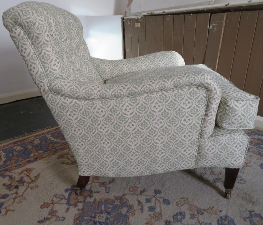 A side profile of a Bridgewater armchair upholstered in green and off-white patterned fabric with dark wooden legs and brass castors.