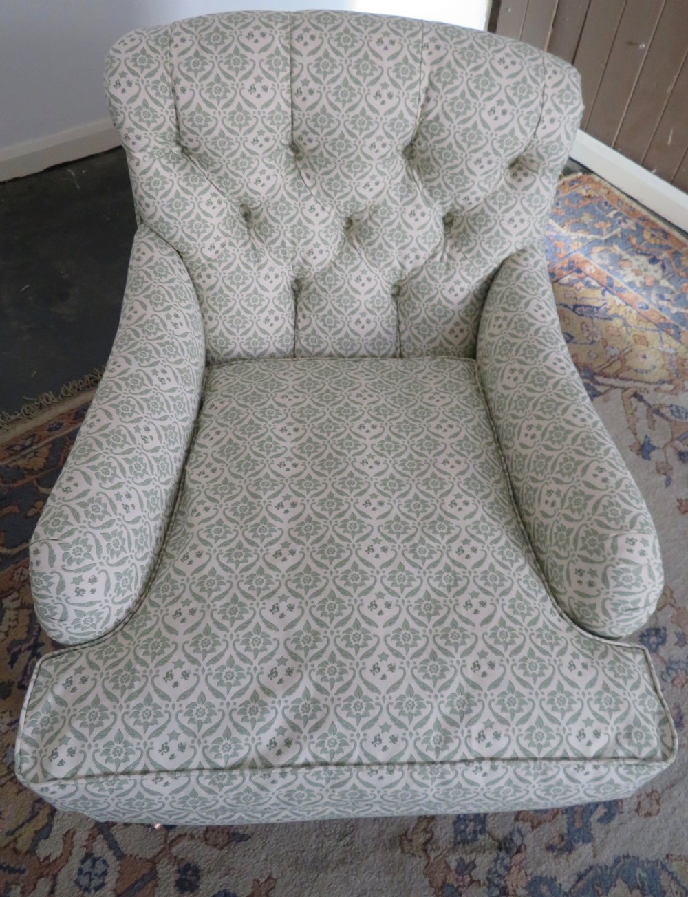 A side profile of a Bridgewater armchair upholstered in green and off-white patterned fabric with dark wooden legs and brass castors. View III