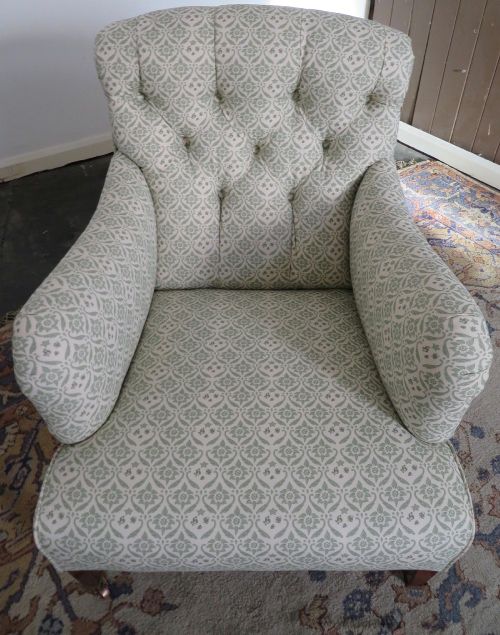 A side profile of a Bridgewater armchair upholstered in green and off-white patterned fabric with dark wooden legs and brass castors. View V