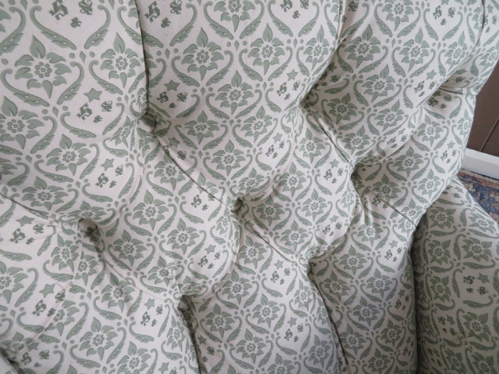 A side profile of a Bridgewater armchair upholstered in green and off-white patterned fabric with dark wooden legs and brass castors. View VI