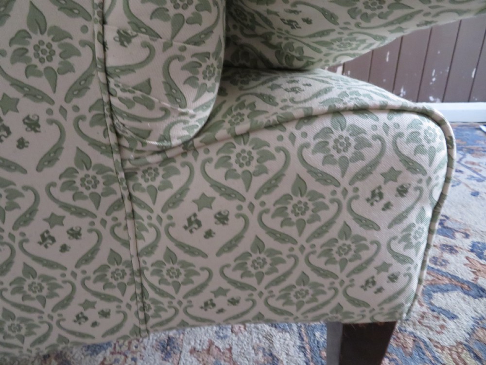 A side profile of a Bridgewater armchair upholstered in green and off-white patterned fabric with dark wooden legs and brass castors. View VIII