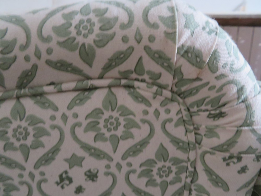 A side profile of a Bridgewater armchair upholstered in green and off-white patterned fabric with dark wooden legs and brass castors. View IX