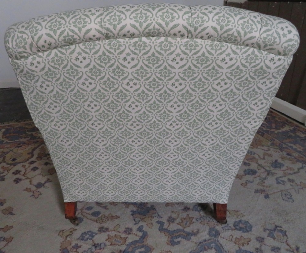 A side profile of a Bridgewater armchair upholstered in green and off-white patterned fabric with dark wooden legs and brass castors. View X