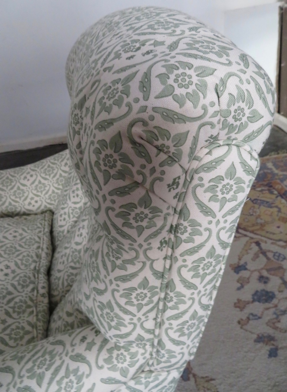 A side profile of a Bridgewater armchair upholstered in green and off-white patterned fabric with dark wooden legs and brass castors. View XIII