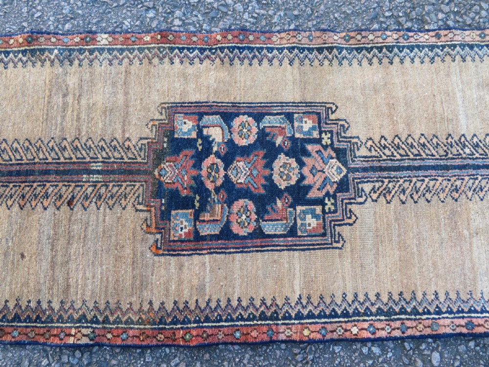 A long, narrow hand-knotted antique Persian Kurdish wool runner rug with geometric central column motifs on a camel field bordered in dark navy blue. View III