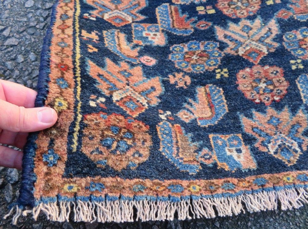 A long, narrow hand-knotted antique Persian Kurdish wool runner rug with geometric central column motifs on a camel field bordered in dark navy blue. View VII