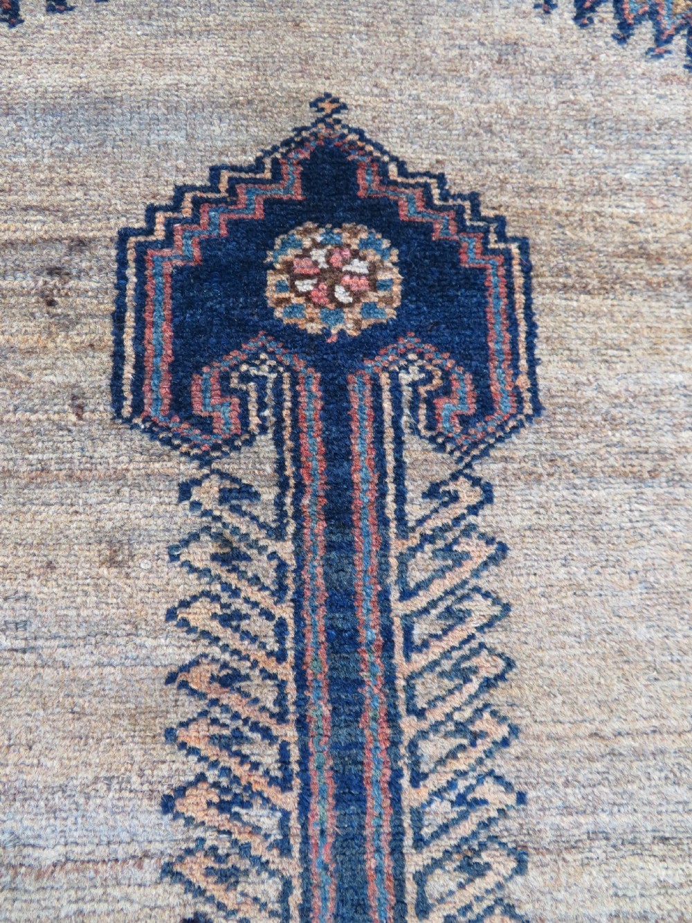 A long, narrow hand-knotted antique Persian Kurdish wool runner rug with geometric central column motifs on a camel field bordered in dark navy blue. View X