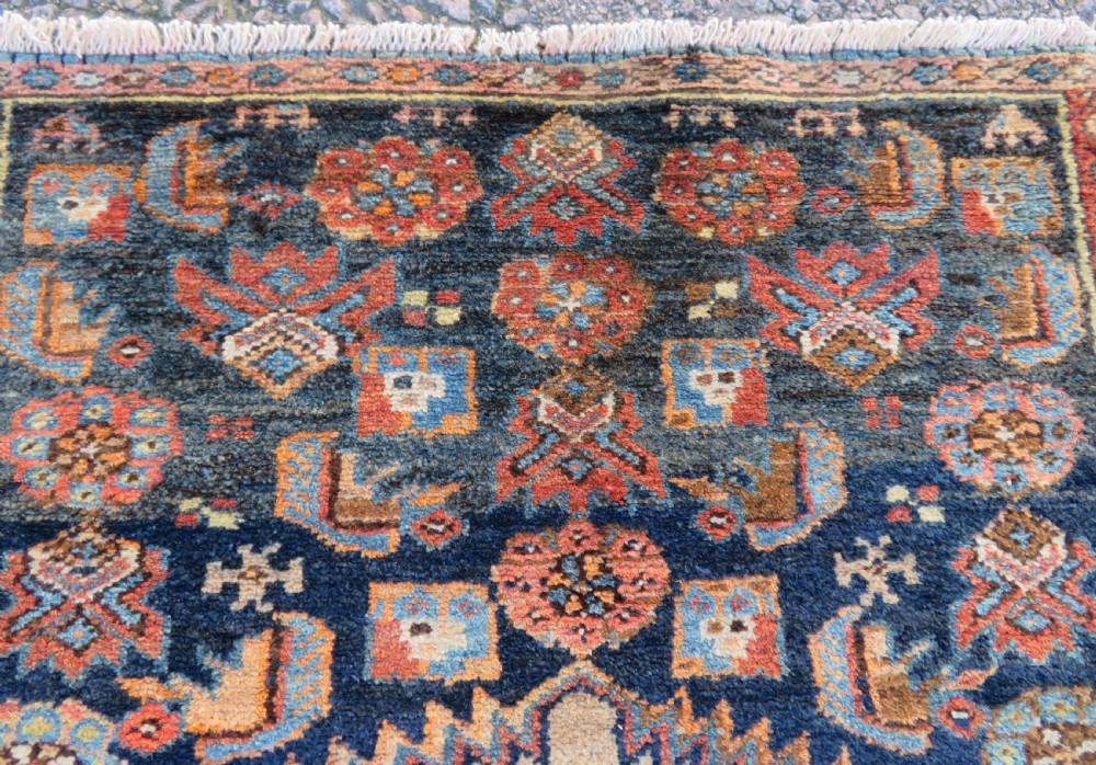 A long, narrow hand-knotted antique Persian Kurdish wool runner rug with geometric central column motifs on a camel field bordered in dark navy blue. View XII
