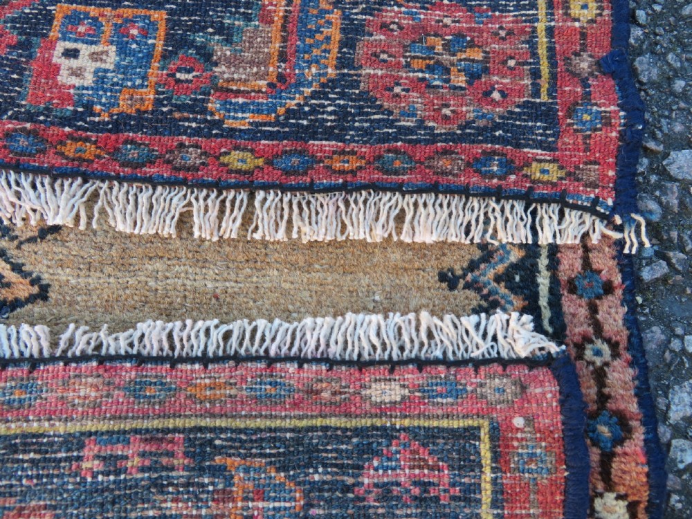 A long, narrow hand-knotted antique Persian Kurdish wool runner rug with geometric central column motifs on a camel field bordered in dark navy blue. View XIV
