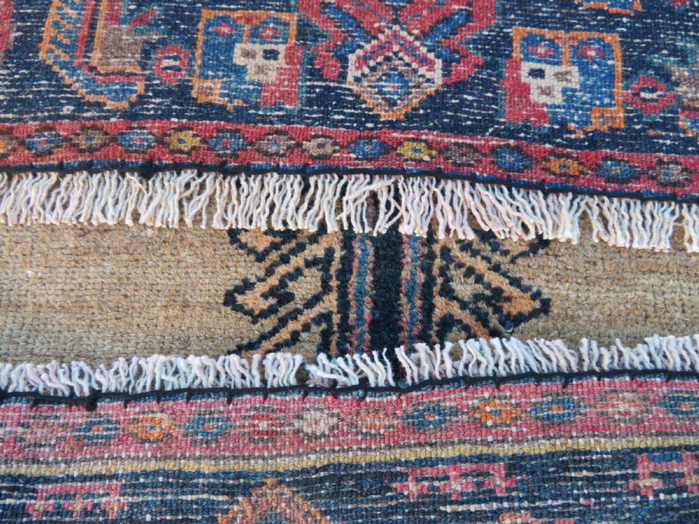 A long, narrow hand-knotted antique Persian Kurdish wool runner rug with geometric central column motifs on a camel field bordered in dark navy blue. View XV