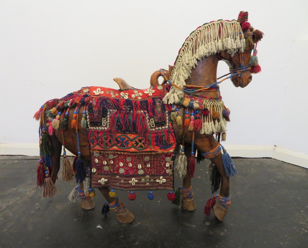 A large carved hardwood model of a standing horse decorated with detailed woven textiles, tassels, and cowrie shells. View VI