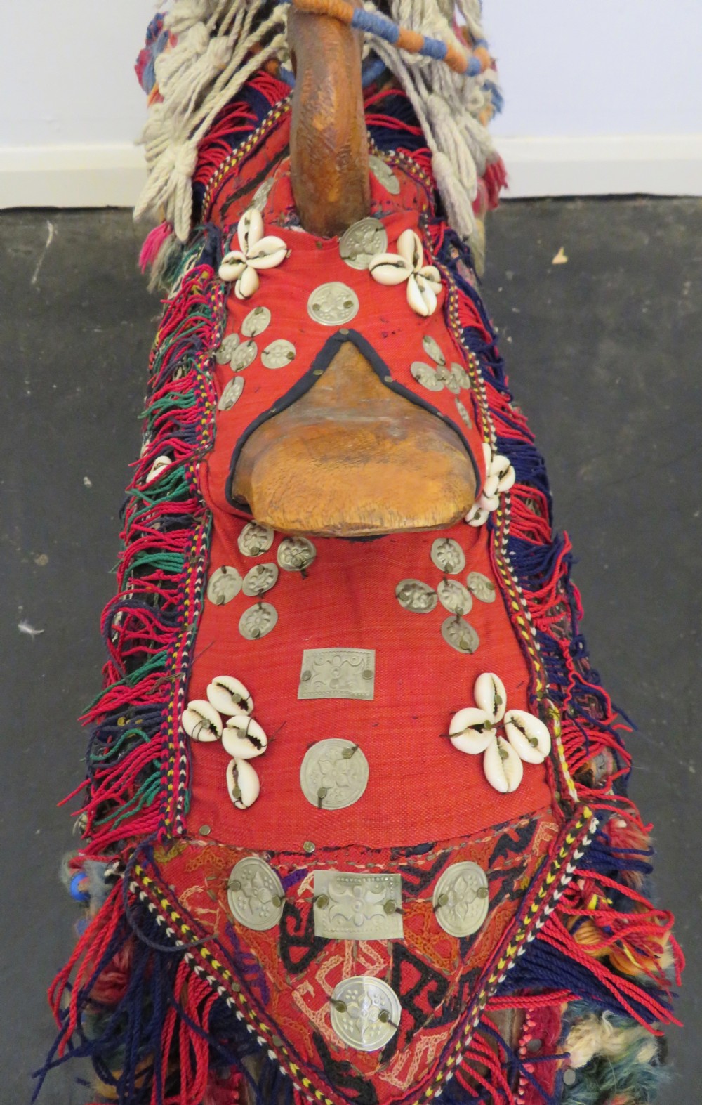A large carved hardwood model of a standing horse decorated with detailed woven textiles, tassels, and cowrie shells. View IX