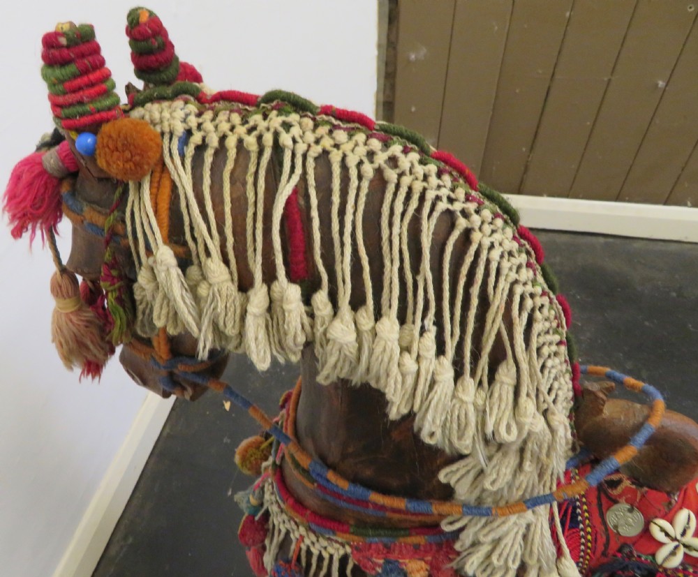 A large carved hardwood model of a standing horse decorated with detailed woven textiles, tassels, and cowrie shells. View X