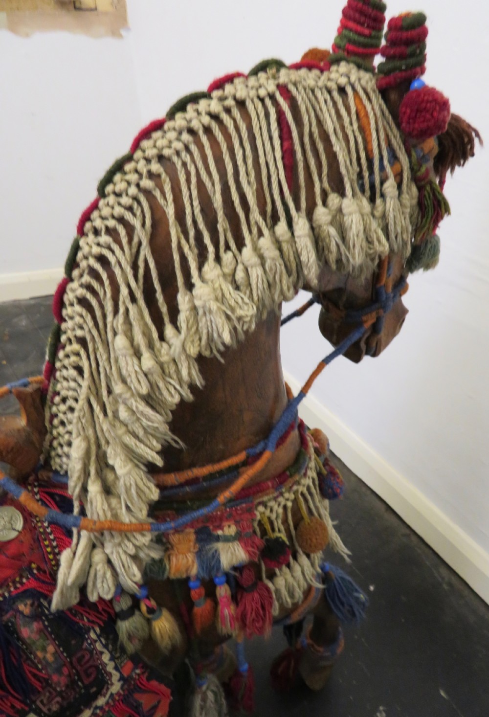 A large carved hardwood model of a standing horse decorated with detailed woven textiles, tassels, and cowrie shells. View XV