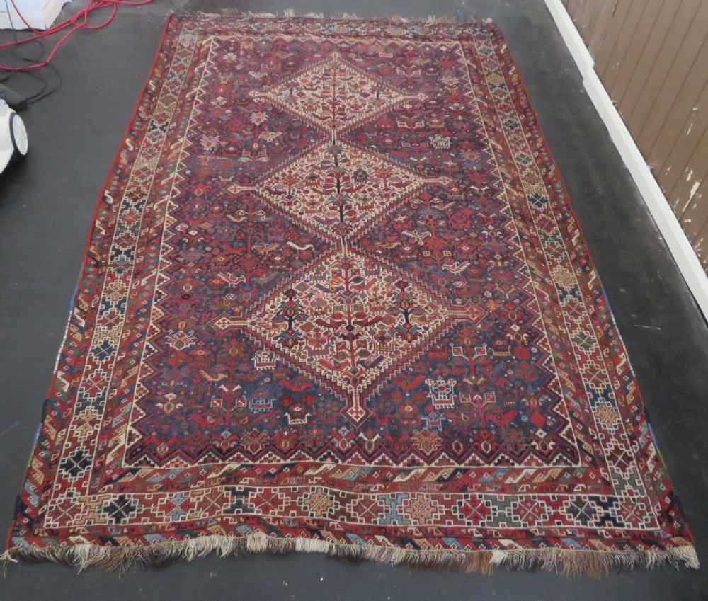 An antique hand-knotted Persian Khamseh rug featuring three diamond central medallions and bird motifs in deep red, navy, cream, and terracotta tones.