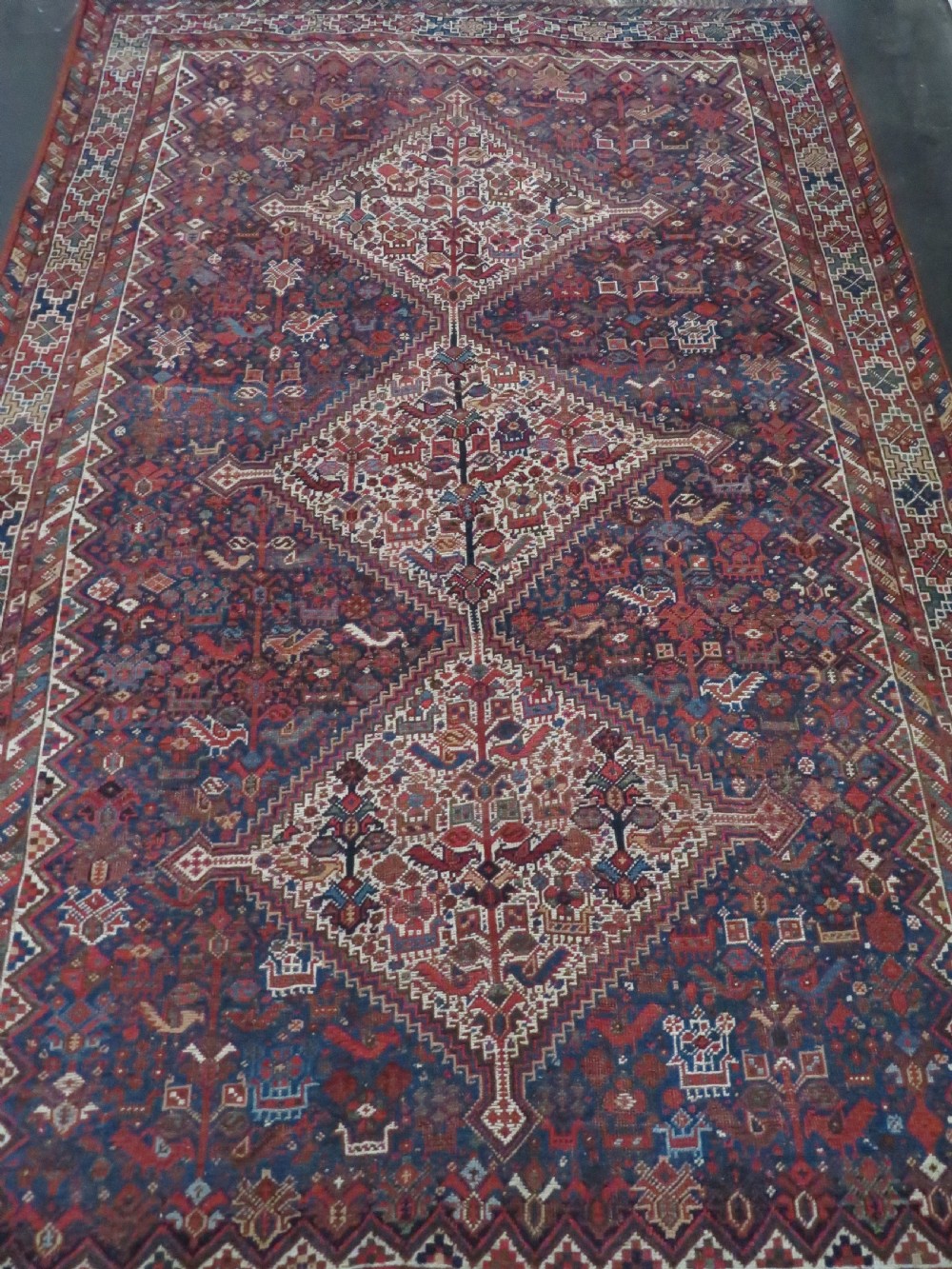 An antique hand-knotted Persian Khamseh rug featuring three diamond central medallions and bird motifs in deep red, navy, cream, and terracotta tones. View II