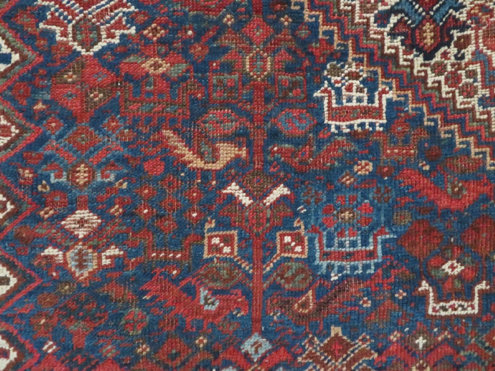 An antique hand-knotted Persian Khamseh rug featuring three diamond central medallions and bird motifs in deep red, navy, cream, and terracotta tones. View VII