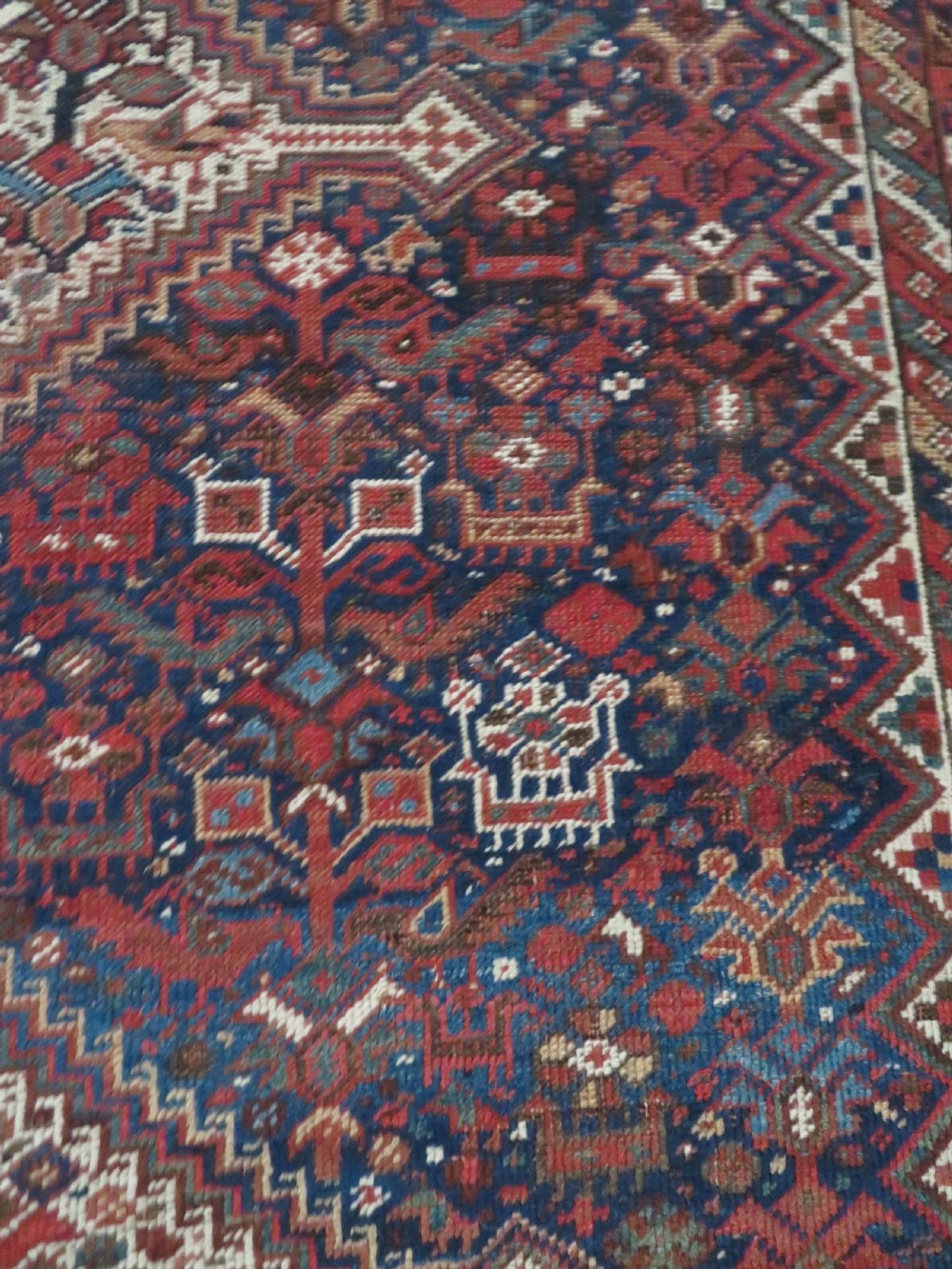 An antique hand-knotted Persian Khamseh rug featuring three diamond central medallions and bird motifs in deep red, navy, cream, and terracotta tones. View IX