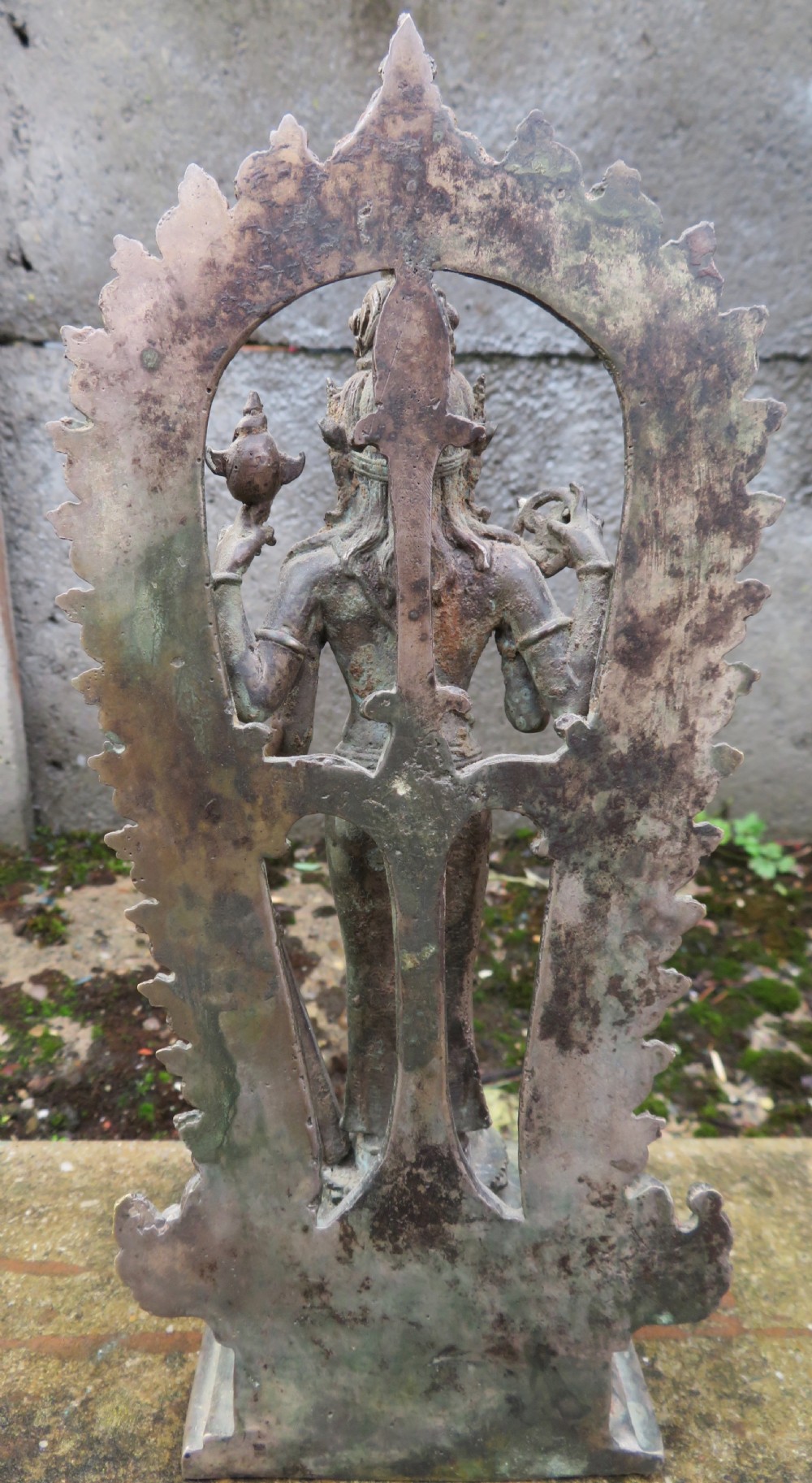 An ancient cast metal figure of Vishnu standing within a flame-edged aureole on a lotus base above a small figure. View XII