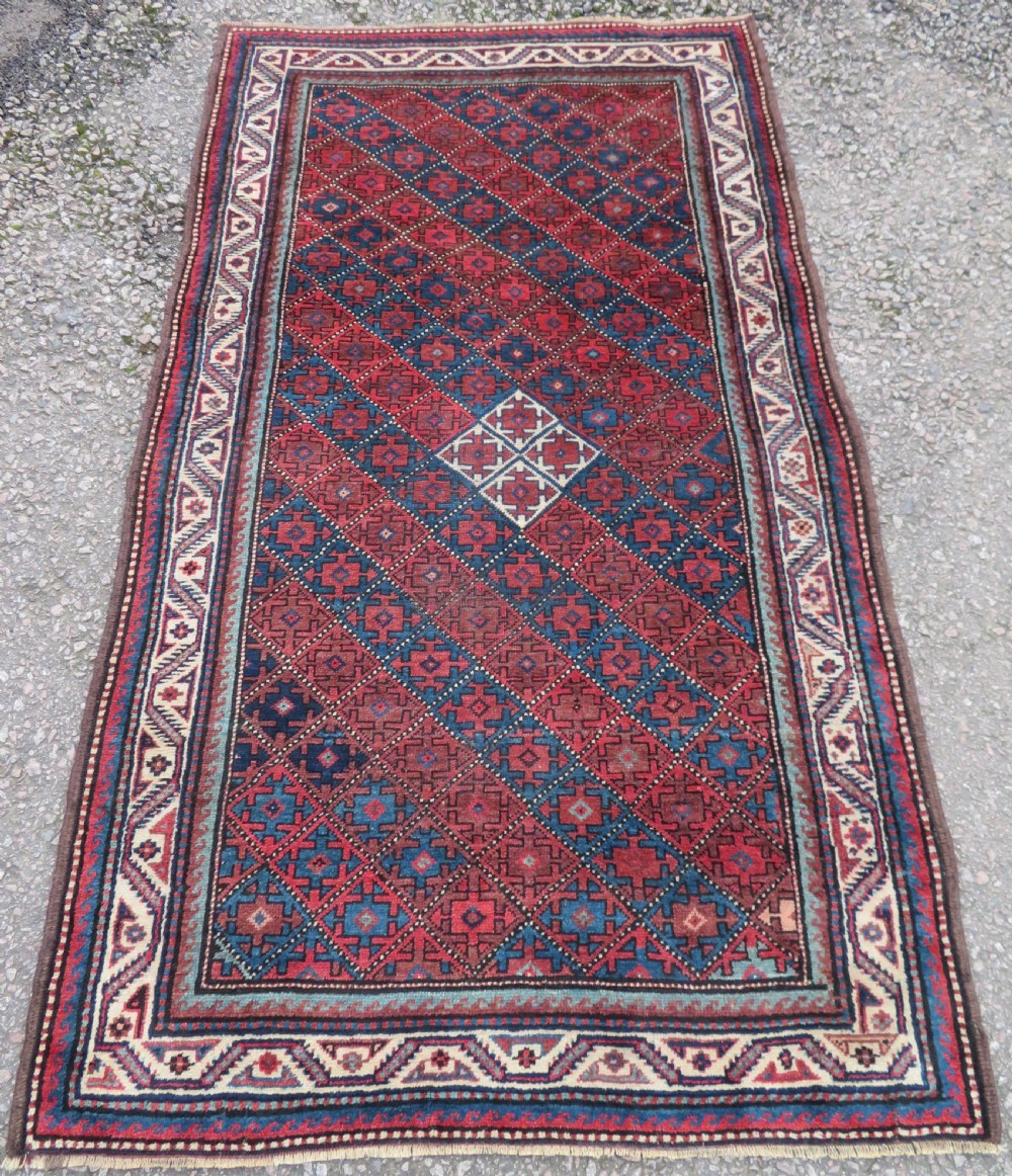 An antique hand-knotted Quchan Kurdish wool rug displaying a central diamond pattern inside a dark red and navy lattice grid with geometric borders.
