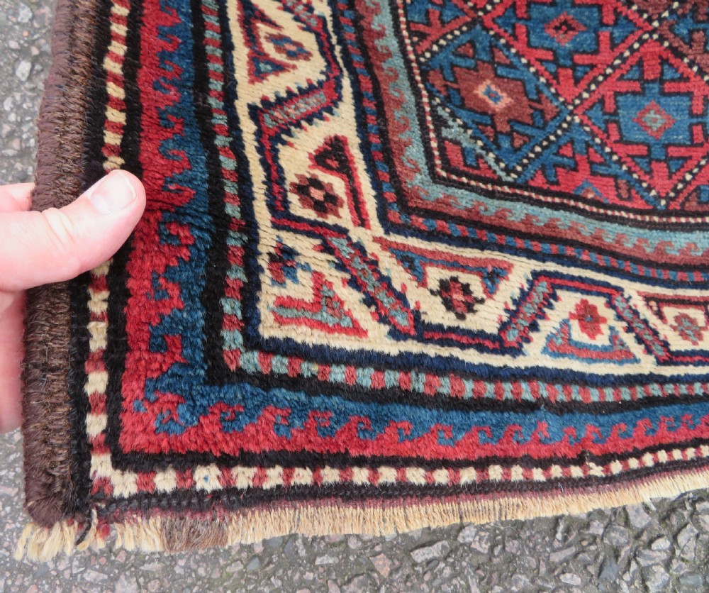 An antique hand-knotted Quchan Kurdish wool rug displaying a central diamond pattern inside a dark red and navy lattice grid with geometric borders. View V