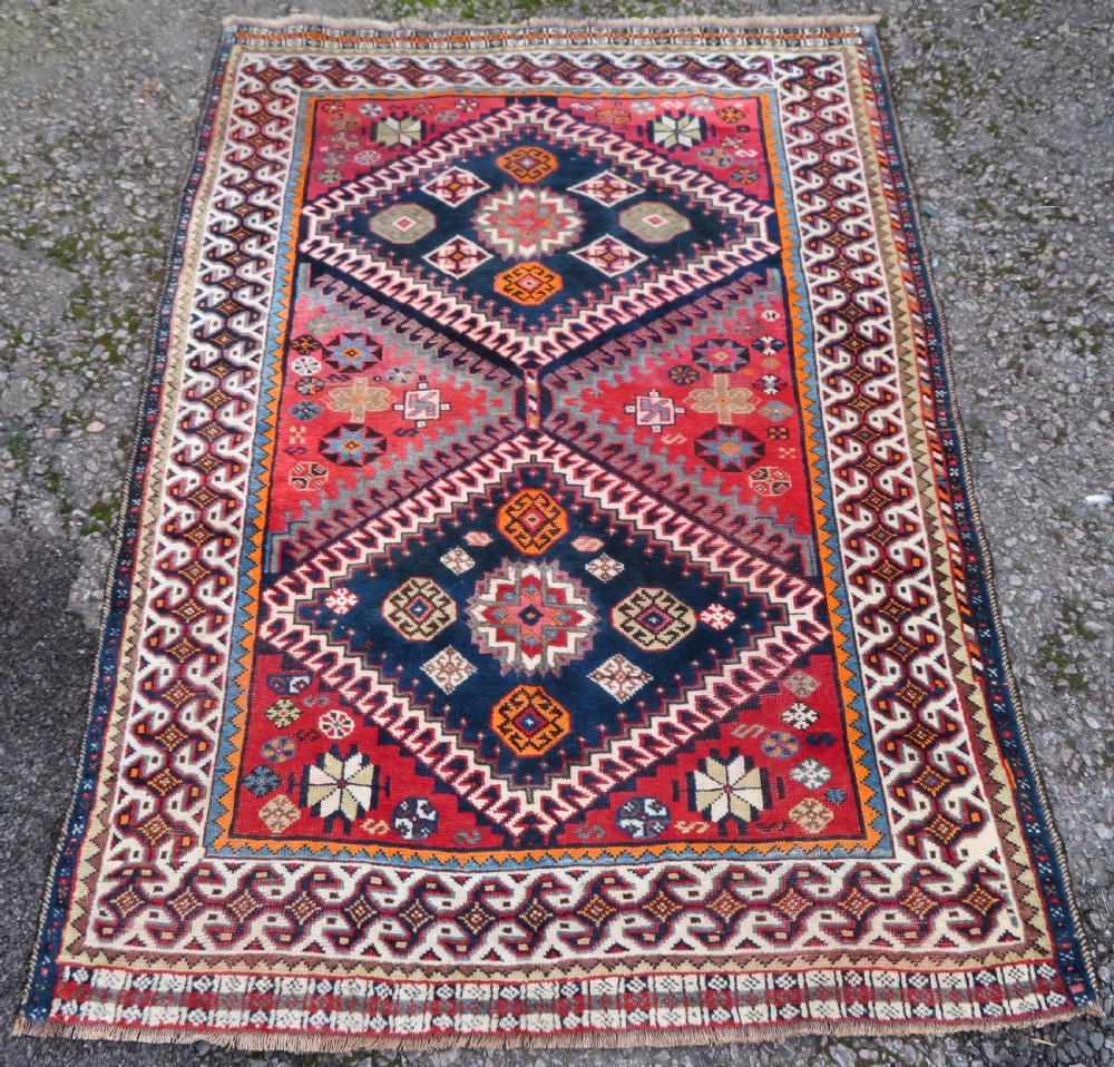 A handwoven Luri tribal rug featuring double geometric diamond medallions in navy blue and red with multi-layered patterned borders.