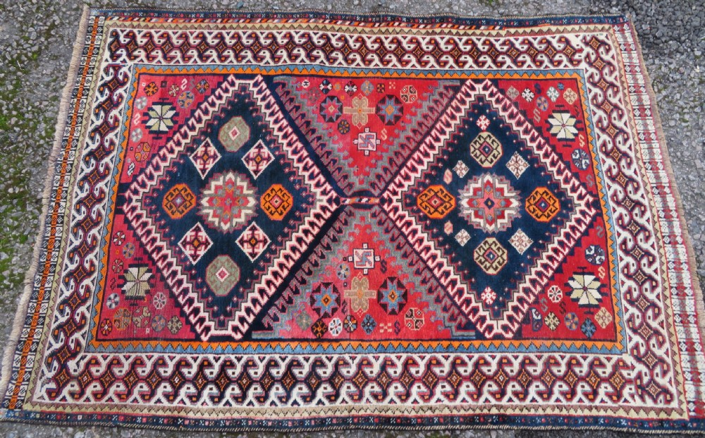 A handwoven Luri tribal rug featuring double geometric diamond medallions in navy blue and red with multi-layered patterned borders. View III