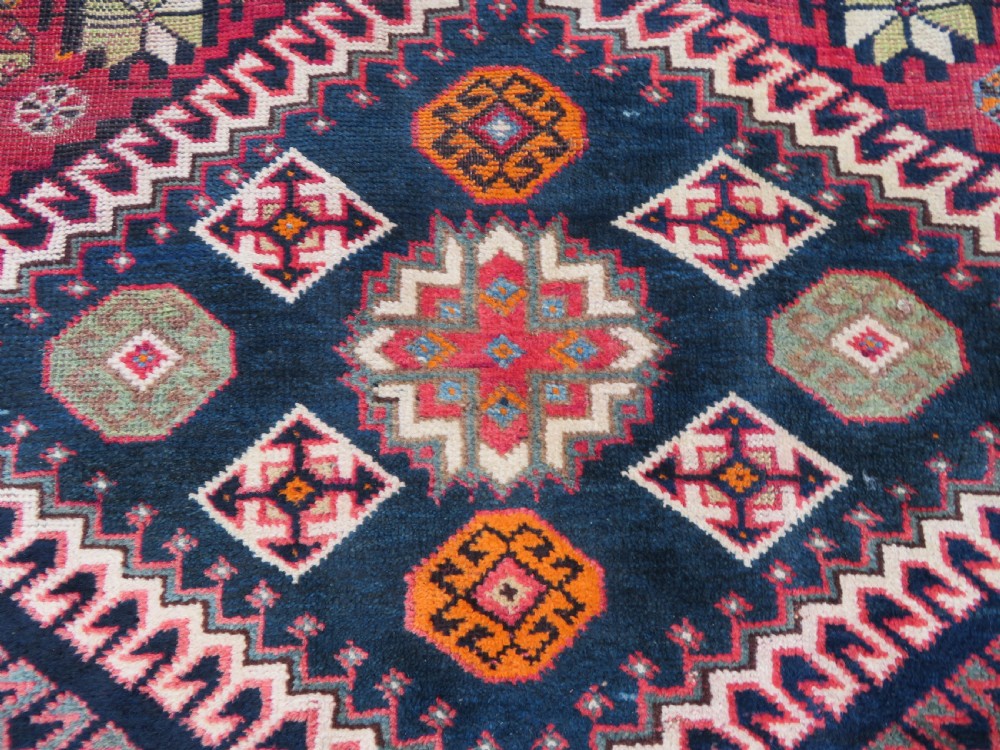 A handwoven Luri tribal rug featuring double geometric diamond medallions in navy blue and red with multi-layered patterned borders. View V