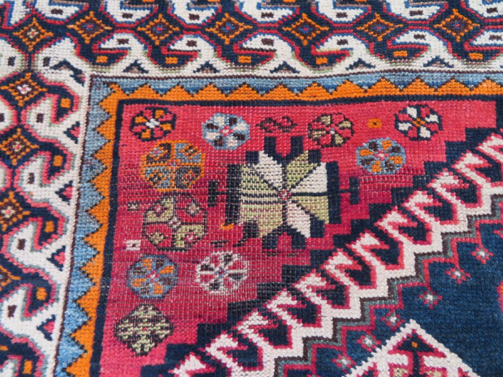 A handwoven Luri tribal rug featuring double geometric diamond medallions in navy blue and red with multi-layered patterned borders. View XI